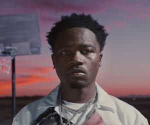 Roddy Ricch stands in front of basketball hoop and pink sky 